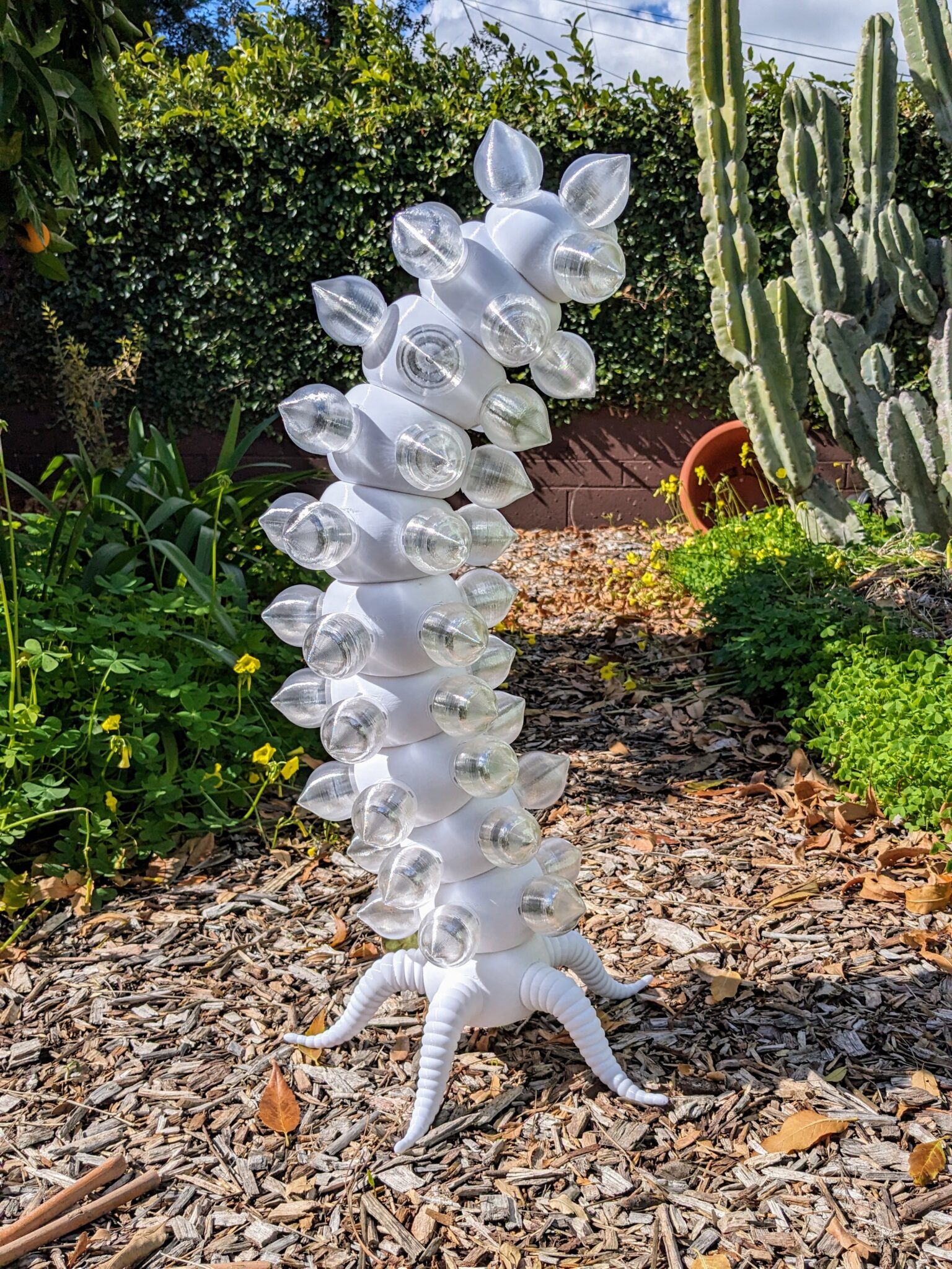 The biomorphic light sculpture "Electric Fireworm" in a sunny garden.